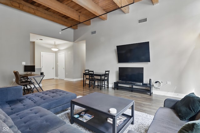 living area featuring wooden ceiling, beam ceiling, wood finished floors, baseboards, and a high ceiling