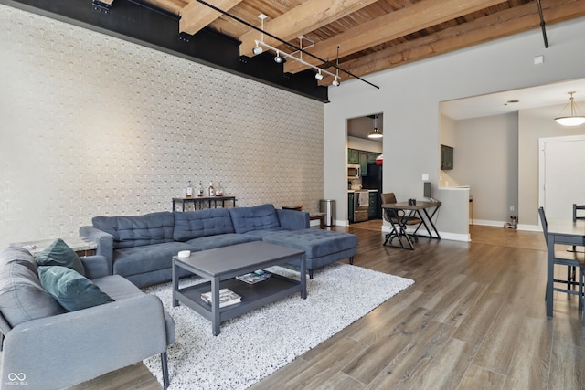 living area featuring wooden ceiling, an accent wall, beam ceiling, baseboards, and wallpapered walls