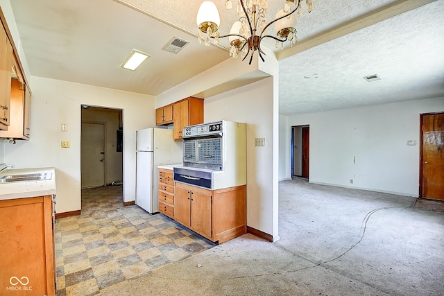 kitchen featuring a notable chandelier, a sink, light countertops, freestanding refrigerator, and baseboards