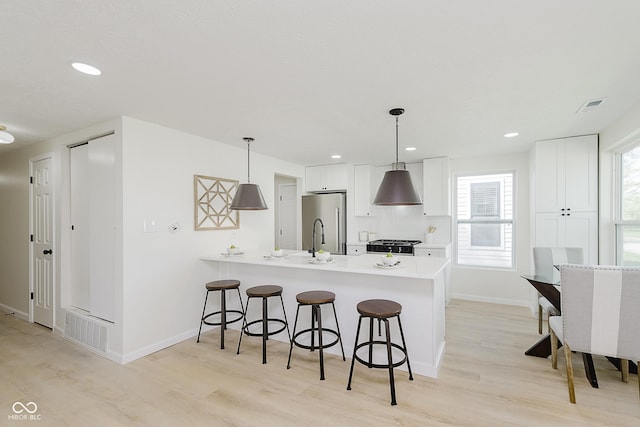 kitchen with a breakfast bar, light wood finished floors, range, freestanding refrigerator, and a peninsula