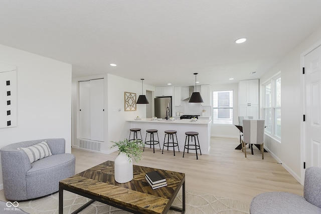 living room featuring light wood-style floors, baseboards, recessed lighting, and visible vents