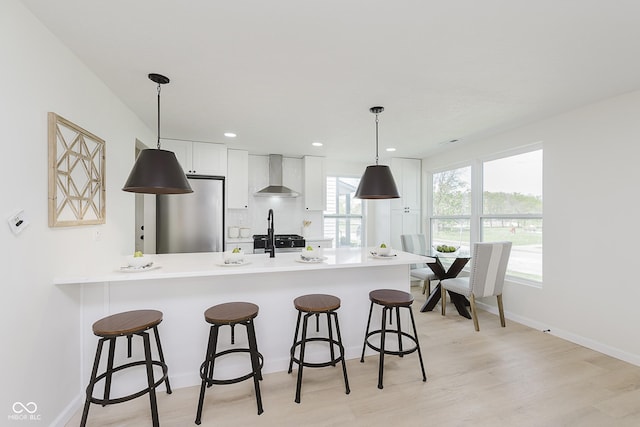 kitchen with a peninsula, refrigerator, a breakfast bar, and wall chimney exhaust hood