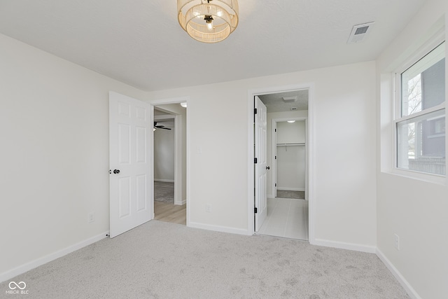 unfurnished bedroom with visible vents, carpet, a walk in closet, and baseboards