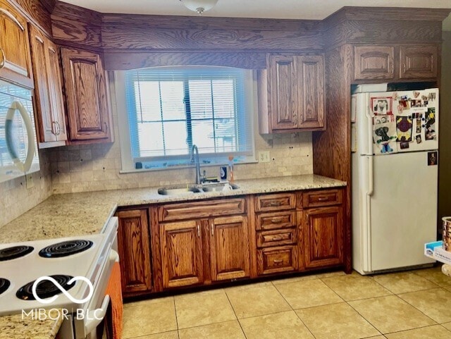 kitchen with brown cabinetry, white appliances, tasteful backsplash, a sink, and light tile patterned floors