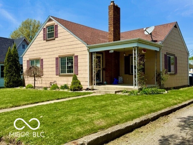 rear view of house with covered porch, a lawn, and a chimney