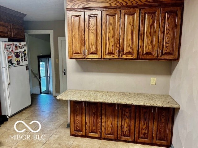 kitchen with freestanding refrigerator, light tile patterned floors, and light stone countertops
