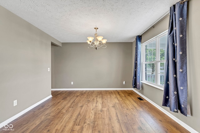unfurnished room with a chandelier, wood finished floors, baseboards, and visible vents