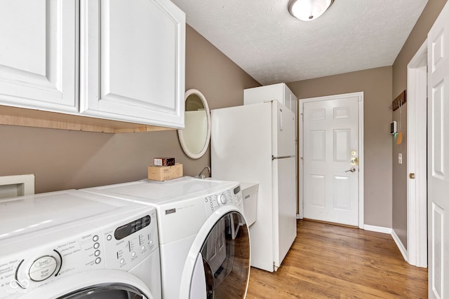 laundry area with washing machine and clothes dryer, cabinet space, light wood-type flooring, and a textured ceiling