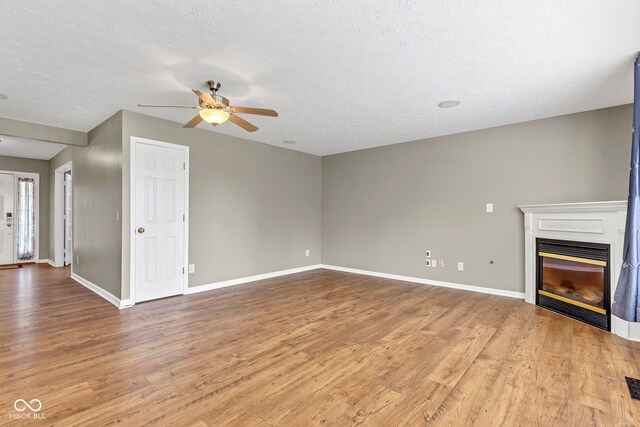 unfurnished living room with wood finished floors, baseboards, ceiling fan, and a glass covered fireplace