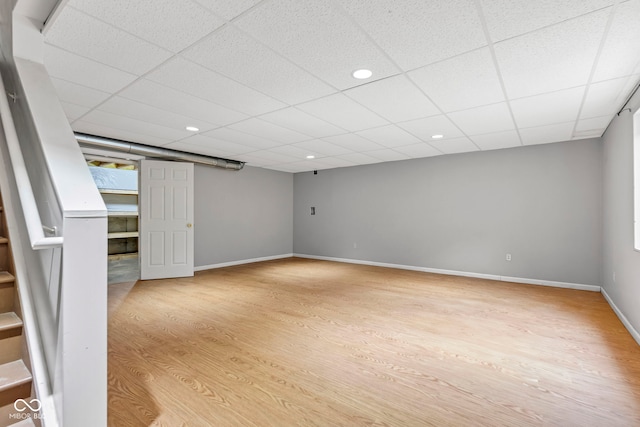 finished below grade area featuring a drop ceiling, light wood-style flooring, baseboards, and recessed lighting