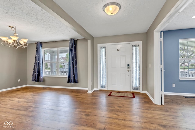 foyer featuring plenty of natural light, a textured ceiling, baseboards, an inviting chandelier, and hardwood / wood-style floors