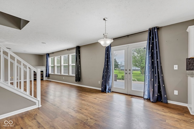 unfurnished living room with stairway, french doors, wood-type flooring, and a textured ceiling