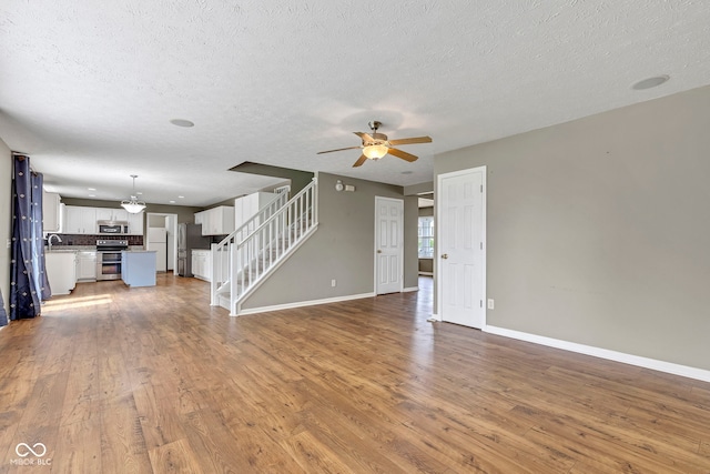 unfurnished living room featuring baseboards, stairs, ceiling fan, and wood finished floors