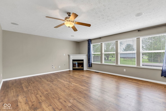 unfurnished living room with a textured ceiling, baseboards, ceiling fan, and a glass covered fireplace