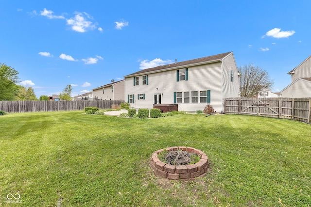 rear view of house with a lawn, a fire pit, and a fenced backyard