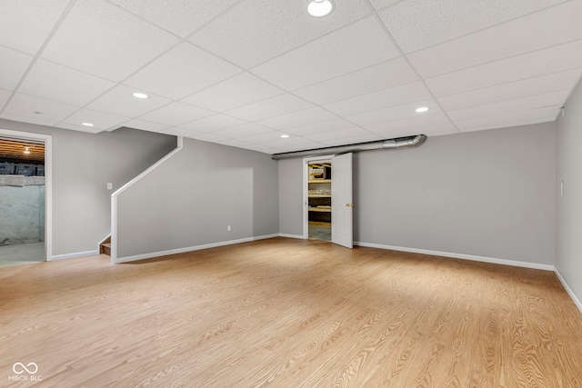 finished below grade area with baseboards, stairs, a drop ceiling, and wood finished floors