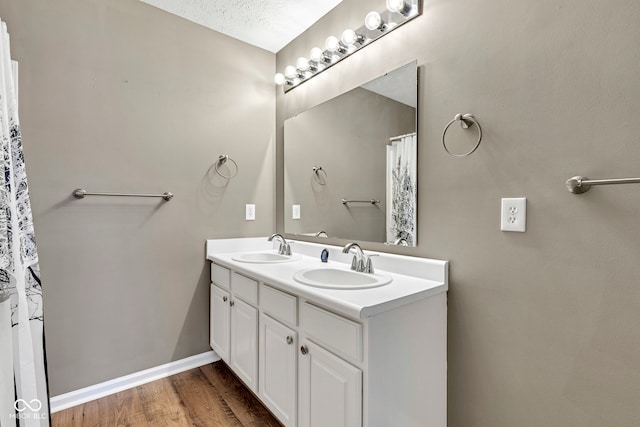 full bathroom featuring baseboards, double vanity, a sink, and wood finished floors