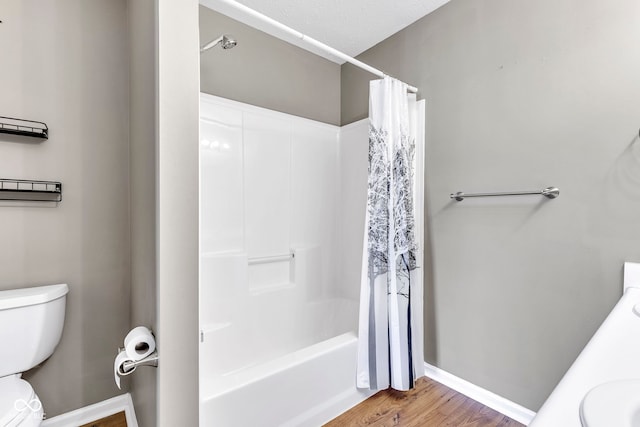 bathroom with toilet, baseboards, shower / bath combination with curtain, a sink, and wood finished floors