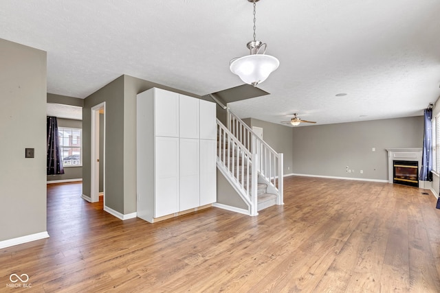 unfurnished living room featuring baseboards, stairs, light wood-style floors, and ceiling fan