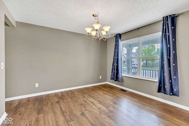 unfurnished room with a textured ceiling, a chandelier, wood finished floors, and baseboards