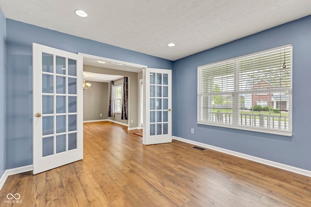 spare room featuring a chandelier, a textured ceiling, baseboards, and french doors