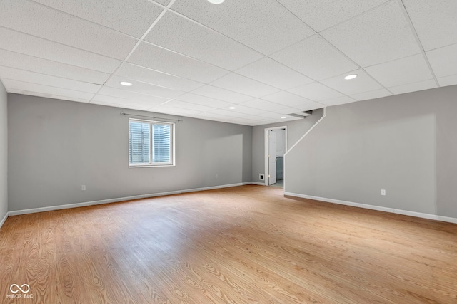 below grade area featuring a paneled ceiling, baseboards, and wood finished floors