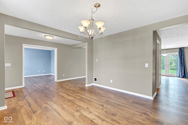 spare room with a chandelier, a textured ceiling, baseboards, and wood finished floors