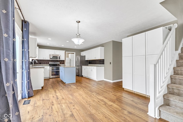 kitchen with a sink, white cabinets, light wood-style floors, stainless steel appliances, and tasteful backsplash