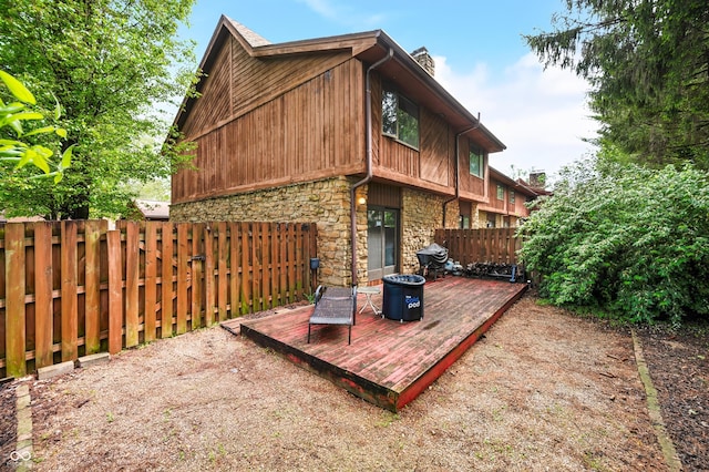 back of property with a chimney, a fenced backyard, stone siding, and a deck