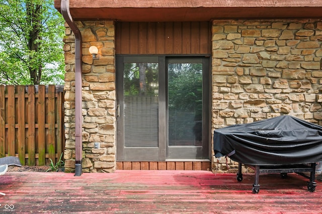 view of exterior entry featuring fence, a wooden deck, and stone siding