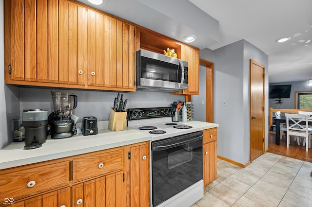 kitchen featuring light tile patterned floors, stainless steel microwave, range with electric stovetop, and brown cabinetry