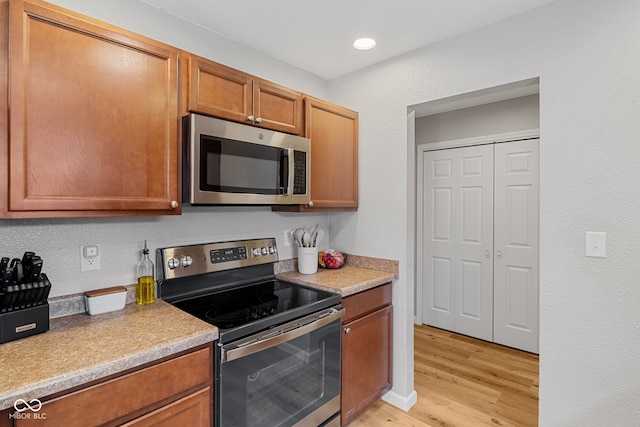 kitchen featuring light wood-style floors, appliances with stainless steel finishes, brown cabinetry, and light countertops