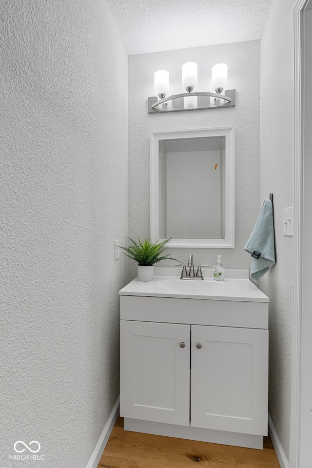 bathroom with wood finished floors, a textured wall, baseboards, and vanity