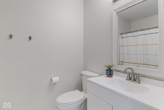 full bath with toilet, a textured wall, and vanity