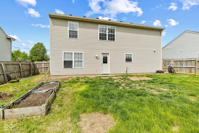 back of house featuring a lawn, a fenced backyard, and a garden