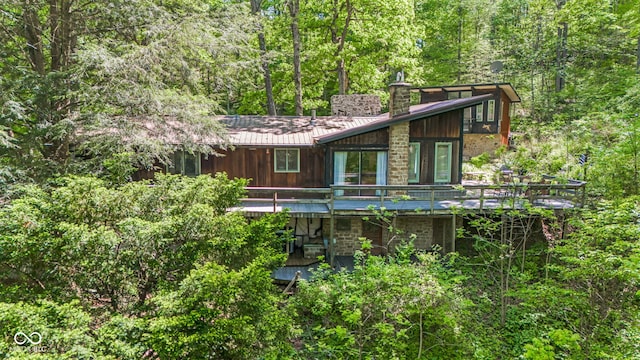 1686 Borders Rd, Nashville, IN 47448 - view of front of house featuring a deck, stone siding, a chimney, a view of trees, and metal roof