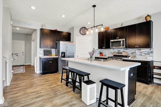 kitchen with a sink, light wood-style floors, a breakfast bar area, stainless steel appliances, and backsplash