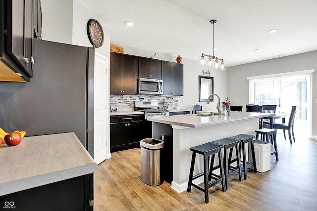 kitchen with a kitchen breakfast bar, a sink, light countertops, stainless steel appliances, and light wood-style flooring