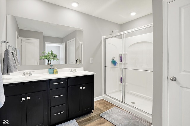 full bath with a sink, double vanity, a shower stall, and wood finished floors