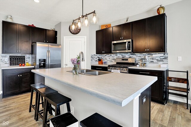 kitchen with stainless steel appliances, tasteful backsplash, a sink, and light wood-type flooring
