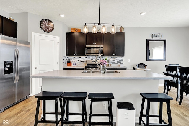 kitchen featuring decorative backsplash, appliances with stainless steel finishes, light countertops, a breakfast bar, and light wood-style flooring