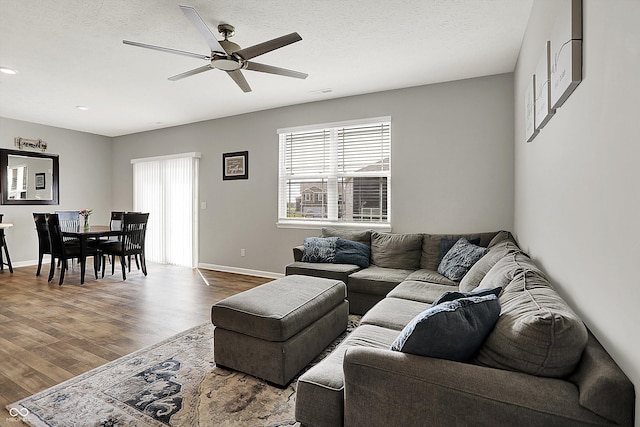 living area with ceiling fan, a wealth of natural light, and wood finished floors