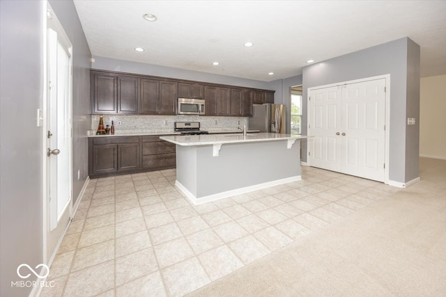 2006 Creek Bank Dr, Columbus, IN 47201 - kitchen with appliances with stainless steel finishes, a sink, light countertops, a center island with sink, and a kitchen bar
