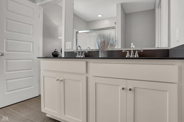 full bathroom featuring double vanity, wood finished floors, recessed lighting, a shower stall, and a sink