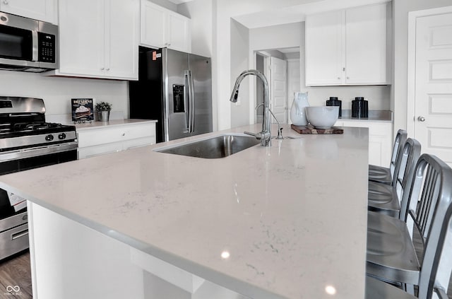 kitchen featuring white cabinets, appliances with stainless steel finishes, a sink, and light stone counters