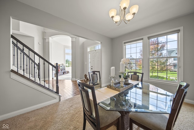 carpeted dining room with baseboards, decorative columns, an inviting chandelier, and stairway
