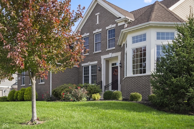 traditional home featuring a shingled roof, a front lawn, and brick siding