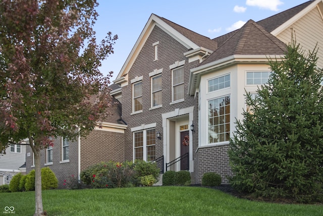 traditional home with brick siding, roof with shingles, and a front yard