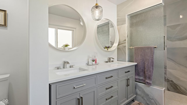 bathroom featuring double vanity, toilet, walk in shower, and a sink