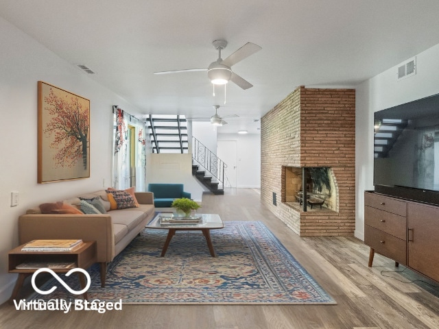 living room featuring ceiling fan, visible vents, a fireplace, wood finished floors, and stairway